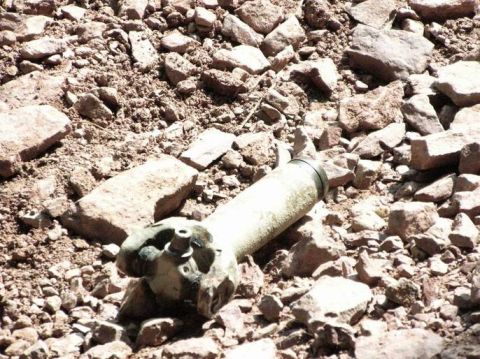1995 Ford Bronco - A piece of unexploded ordnance rests on a surface covered with rocks and debris.