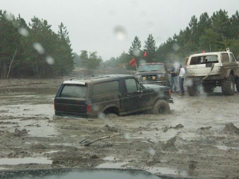 1995 Ford Bronco - Several off-road vehicles are stuck in deep mud during an outdoor event.