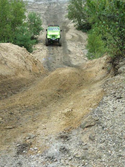 1995 Ford Bronco - A green Jeep Wrangler navigates an off-road trail, climbing a steep dirt incline.