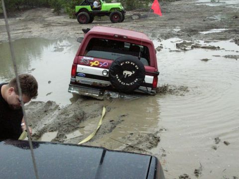 1995 Ford Bronco - A red Ford Bronco is stuck in a muddy puddle, while a green Jeep waits nearby.