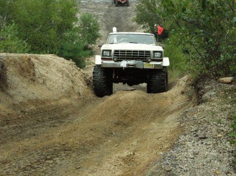 1995 Ford Bronco - White off-road vehicle navigates a steep dirt track, with another vehicle in the distance.