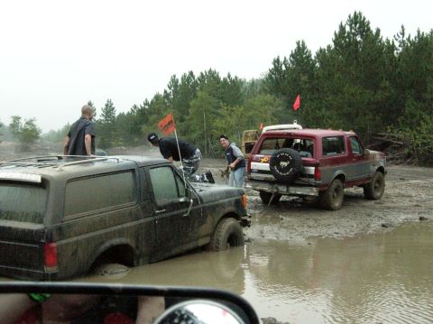 1995 Ford Bronco - Two off-road vehicles are stuck in a muddy area, with people attempting to pull one out.