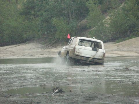 1995 Ford Bronco - A white 1995 Ford Bronco navigates a muddy terrain, kicking up water and mud.