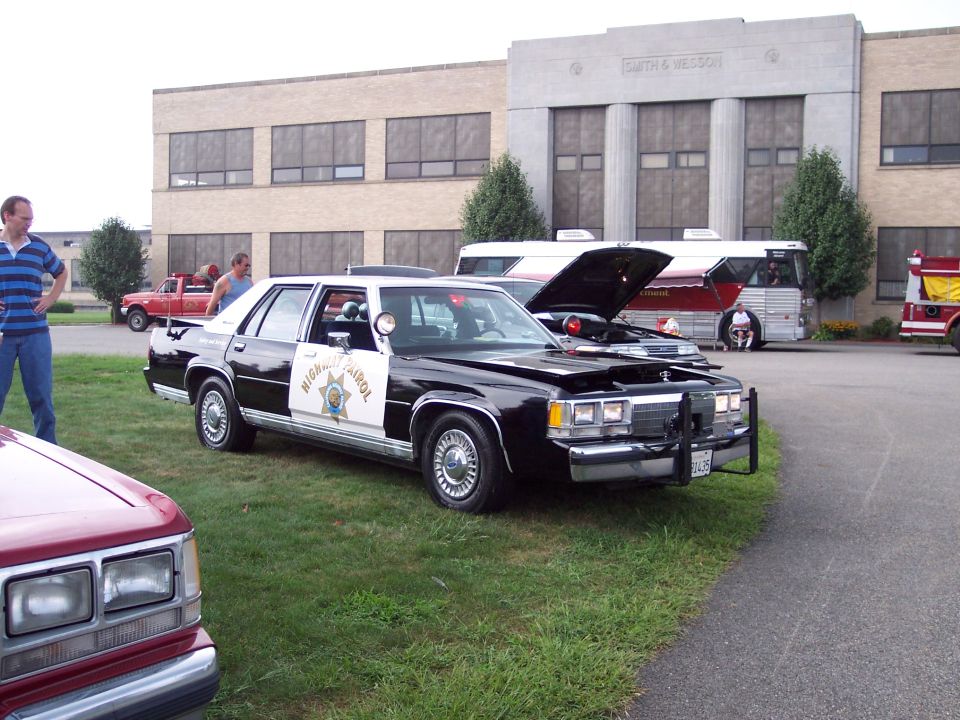 Black and white police car with hood open, "HIGHWAY PATROL" text on door, parked on grass