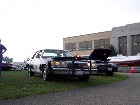 2001 Ford Crown Victoria - A police car with its hood up is parked on grass next to another vehicle.