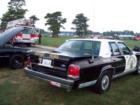 2001 Ford Crown Victoria - Rear view of a 2001 Ford Crown Victoria police car, parked on grass next to a fire truck.
