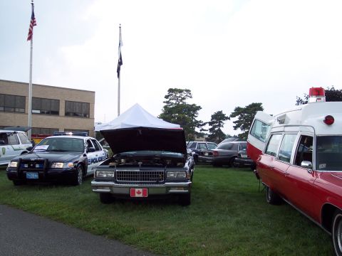 2001 Ford Crown Victoria - A dark 1980s Chevrolet Caprice Classic is displayed with its hood open, alongside a police car and an ambulance.