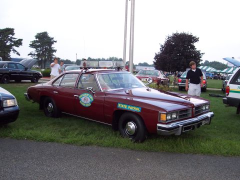 2001 Ford Crown Victoria - A vintage state patrol car is displayed at an outdoor event with other vehicles and tents in the background.