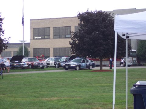 2001 Ford Crown Victoria - A police car, identified as a 2001 Ford Crown Victoria, is parked on a grassy field next to other vehicles.