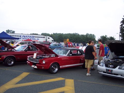 2001 Ford Crown Victoria - Classic red Mustang convertible on display at a car show with other vehicles and spectators.