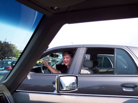 2001 Ford Crown Victoria - A driver waves from inside a 2001 Ford Crown Victoria, with other vehicles visible in the background and side mirror.