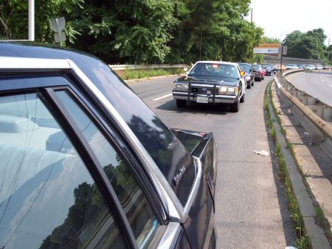 2001 Ford Crown Victoria - A Ford Crown Victoria police car leads a line of vehicles on a highway.