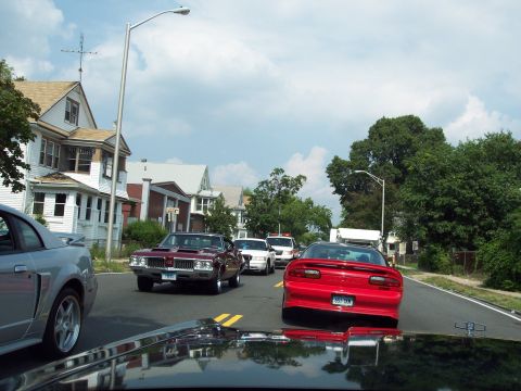2001 Ford Crown Victoria - Several cars are driving down a suburban street on a cloudy day.