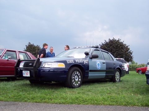 2001 Ford Crown Victoria - A 2001 Ford Crown Victoria police car is parked on grass with other vehicles nearby under a cloudy sky.