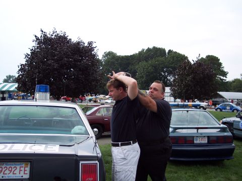 2001 Ford Crown Victoria - Officers apprehend a man next to a police car, with other vehicles visible at an outdoor event.