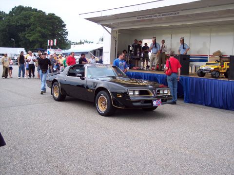 2001 Ford Crown Victoria - A black 1977 Pontiac Trans Am is displayed at an outdoor event with people watching.