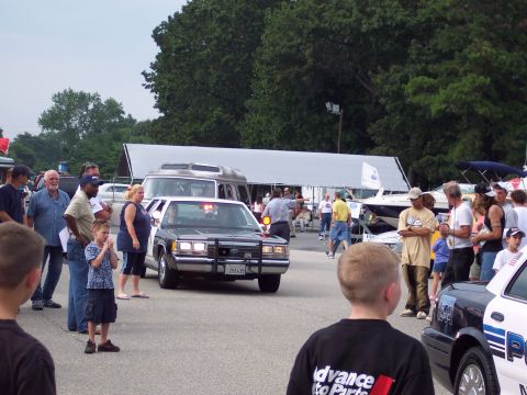 2001 Ford Crown Victoria - A police car is the focus of attention at an outdoor event with many onlookers and other vehicles present.