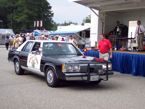 2001 Ford Crown Victoria - A 1998 Ford Crown Victoria police car is displayed at an outdoor event with a stage and crowd in the background.