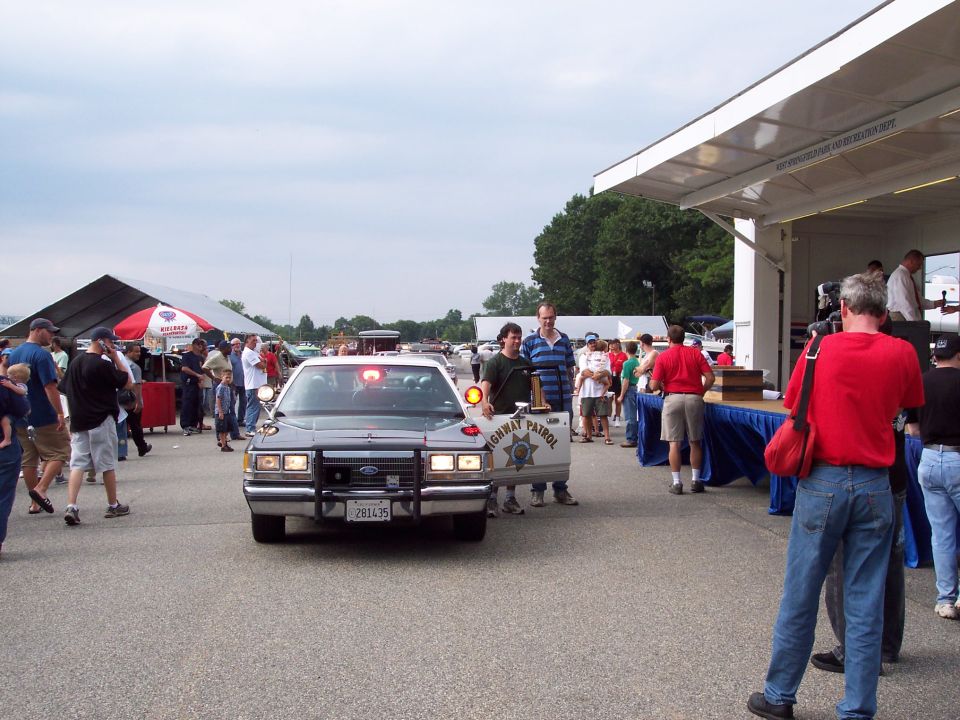 Police car with 'HIGHWAY PATROL' on the door, two men standing beside it