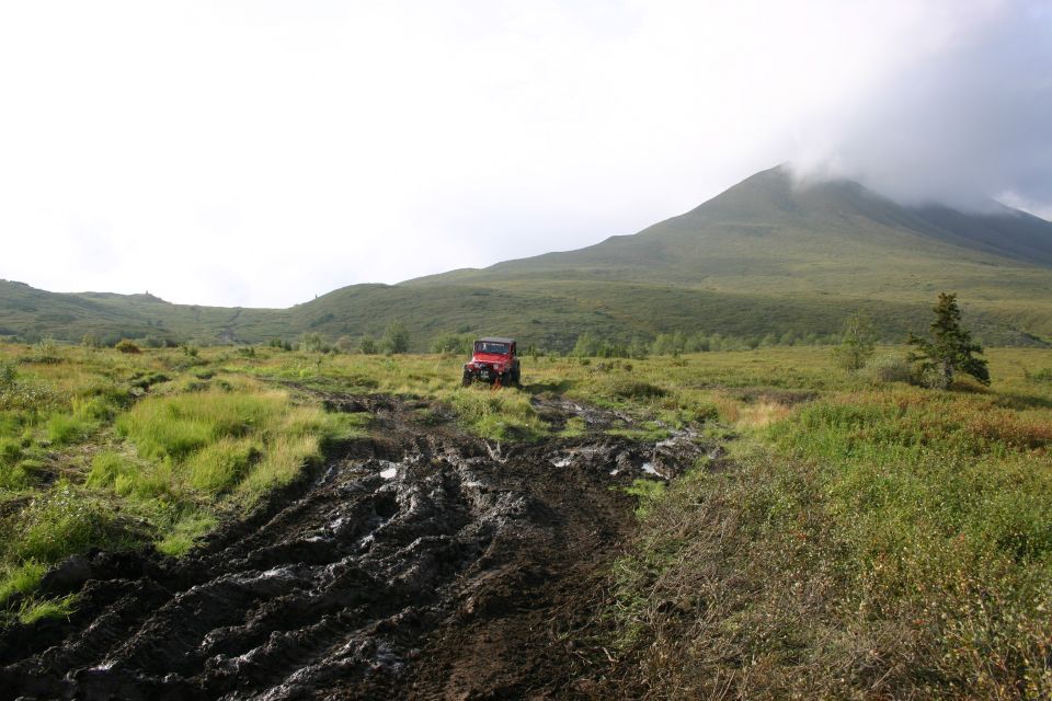 Red Jeep Wrangler on a deeply rutted muddy trail in open tundra with foggy mountains behind