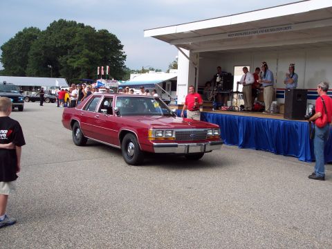 2001 Ford Crown Victoria - A red sedan is displayed in front of a stage at an outdoor event.