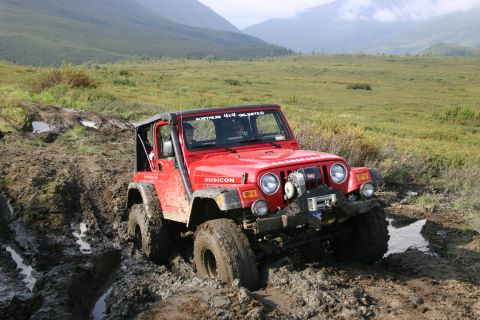 2003 Jeep TJ - Red 2003 Jeep TJ Rubicon navigating a muddy off-road trail with mountains in the background.