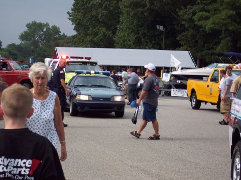 2001 Ford Crown Victoria - A police car, possibly a Ford Mustang, is parked with emergency lights activated at an outdoor event.