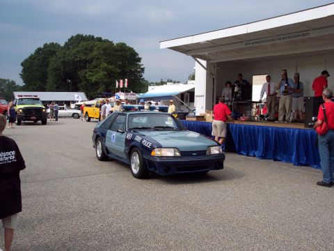 2001 Ford Crown Victoria - A state police car drives past a stage set up for an event.