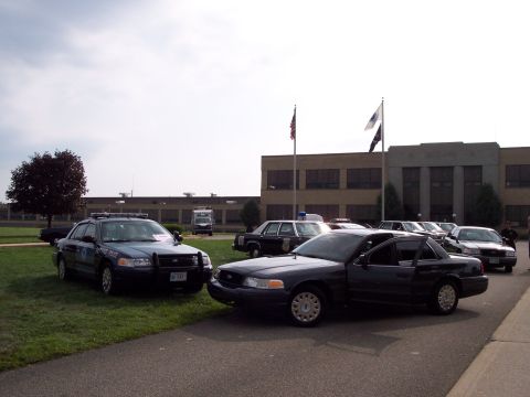 2001 Ford Crown Victoria - Several police Crown Victorias are parked on grass and pavement near a building.