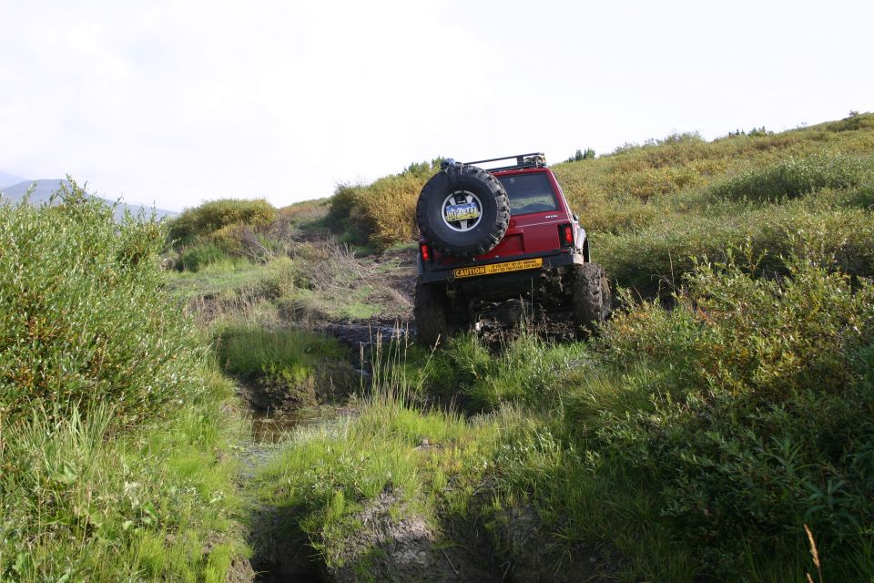 red Jeep Cherokee XJ climbing a muddy hill with a spare tire on the back
