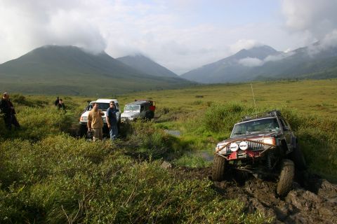 2003 Jeep TJ - Multiple SUVs navigating a muddy off-road trail with mountainous terrain in the background.