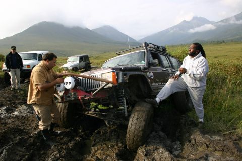 2003 Jeep TJ - Several off-road vehicles are stuck in deep mud on a trail with mountains in the distance.