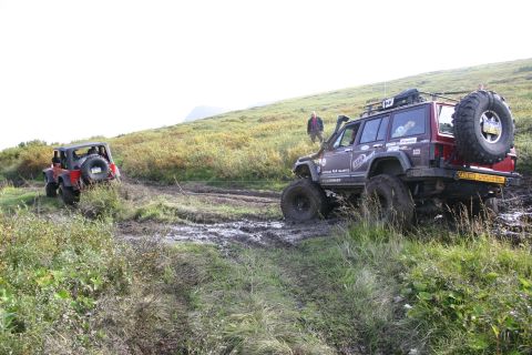 2003 Jeep TJ - Two modified Jeeps navigate a challenging muddy terrain on a grassy slope, their off-road capabilities.
