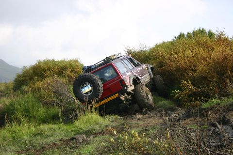 2003 Jeep TJ - A red Jeep Cherokee XJ navigates a steep, muddy incline surrounded by dense vegetation.