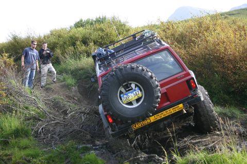 2003 Jeep TJ - A red 2003 Jeep TJ navigates a muddy off-road trail with two onlookers.