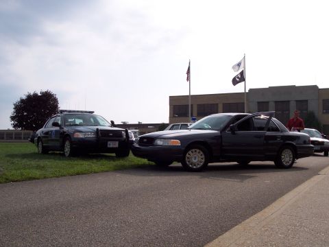 2001 Ford Crown Victoria - Two Ford Crown Victoria police cars are parked outside a building under a cloudy sky.