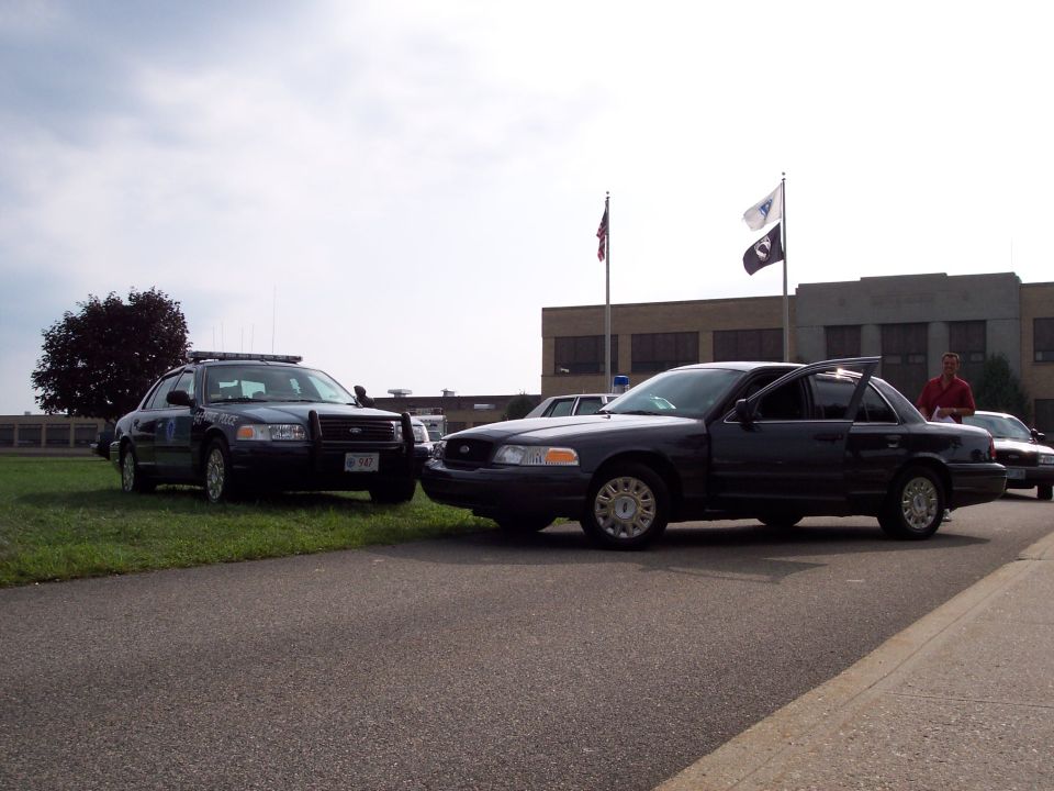 Two dark Ford Crown Victoria police cars parked, one with doors open. 2001 Ford Crown Victoria
