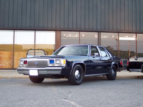 2001 Ford Crown Victoria - A dark blue Ford Crown Victoria police car is parked in front of a building with large windows.