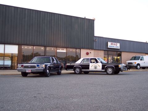 2001 Ford Crown Victoria - Two sedans and a van parked outside MHQ Municipal Supply.