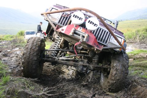2003 Jeep TJ - Modified Jeep Cherokee XJ with winch and IPF lights is stuck deep in mud. Another Jeep is in the background.