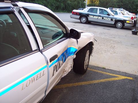 2001 Ford Crown Victoria - A damaged Lowell police car is parked next to other police vehicles, showing significant damage to the front fender and door.
