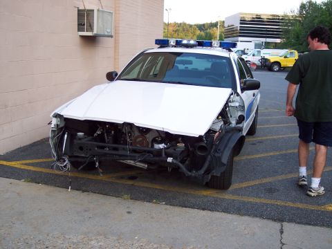 2001 Ford Crown Victoria - A damaged 2001 Ford Crown Victoria police car sits in a parking lot with its front end dismantled.