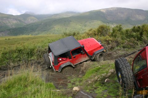 2003 Jeep TJ - A red 2003 Jeep TJ is stuck in a muddy ditch, with another vehicle partially visible to the right.