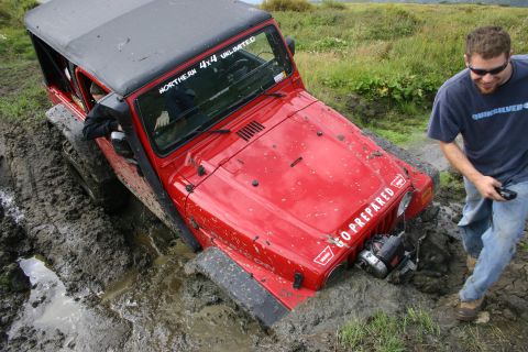2003 Jeep TJ - A red Jeep TJ is deeply stuck in thick mud, with a man observing the situation.