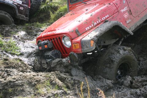2003 Jeep TJ - A red Jeep Wrangler is stuck in thick mud, with another vehicle partially visible behind it.