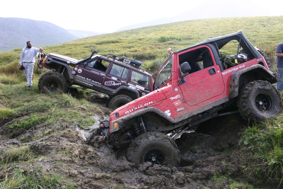 Red doorless Jeep Wrangler Rubicon flexing through a mud hole on a tundra hillside
