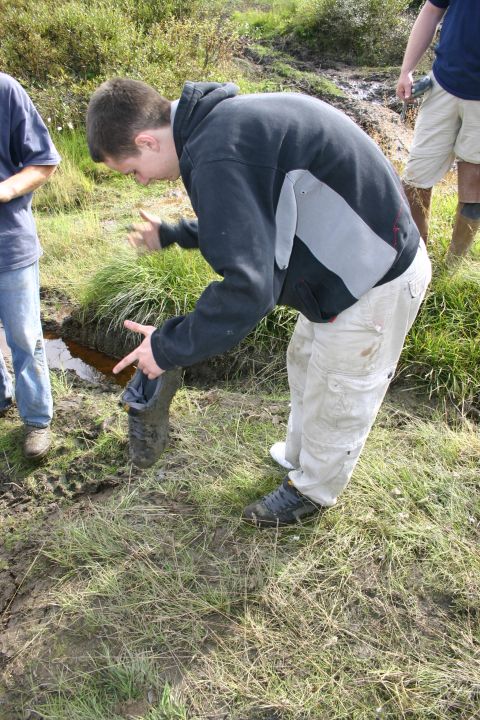 2003 Jeep TJ - A person retrieves a muddy boot from a wet, grassy area with other people nearby.