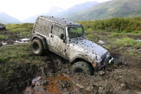 2003 Jeep TJ - A Jeep TJ is deeply stuck in thick mud on an off-road trail, with a second vehicle partially visible in the background.