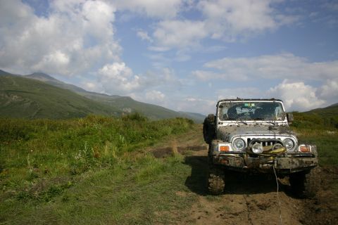 2003 Jeep TJ - A white 2003 Jeep TJ is covered in mud as it sits on a dirt trail with mountains in the background.