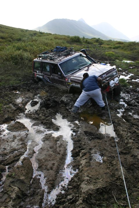 2003 Jeep TJ - A person attempts to free a Jeep Cherokee that is deeply stuck in thick mud.
